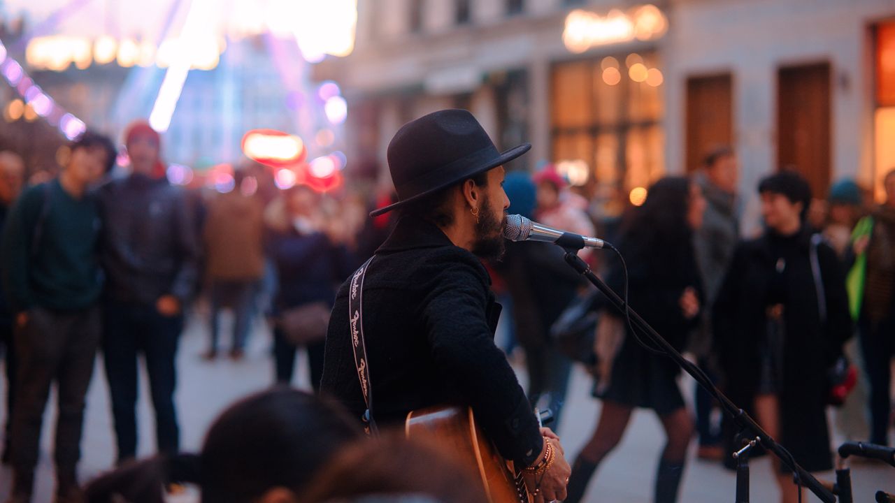 A street musician plays guitar and sings to an engaged crowd in a lively urban setting.
