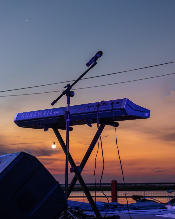 A digital keyboard and microphone set up on an outdoor stage during a vibrant sunset.