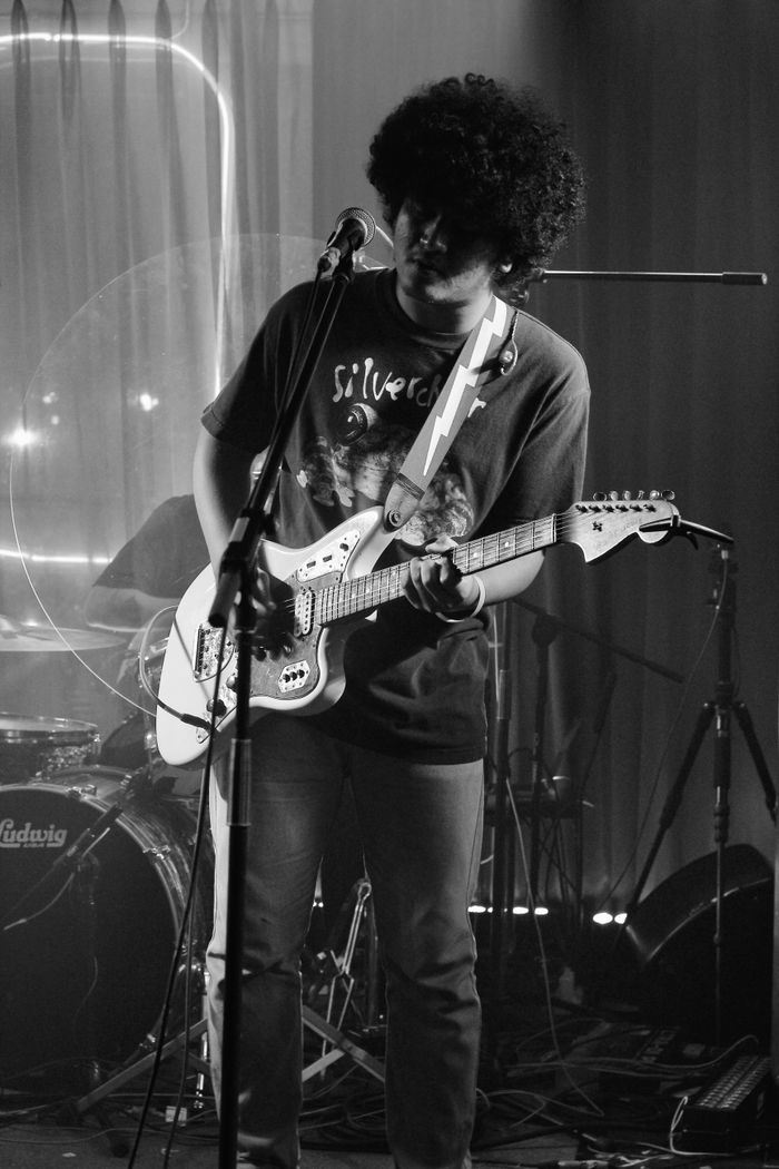 Musician playing electric guitar on stage in moody black and white ambiance.