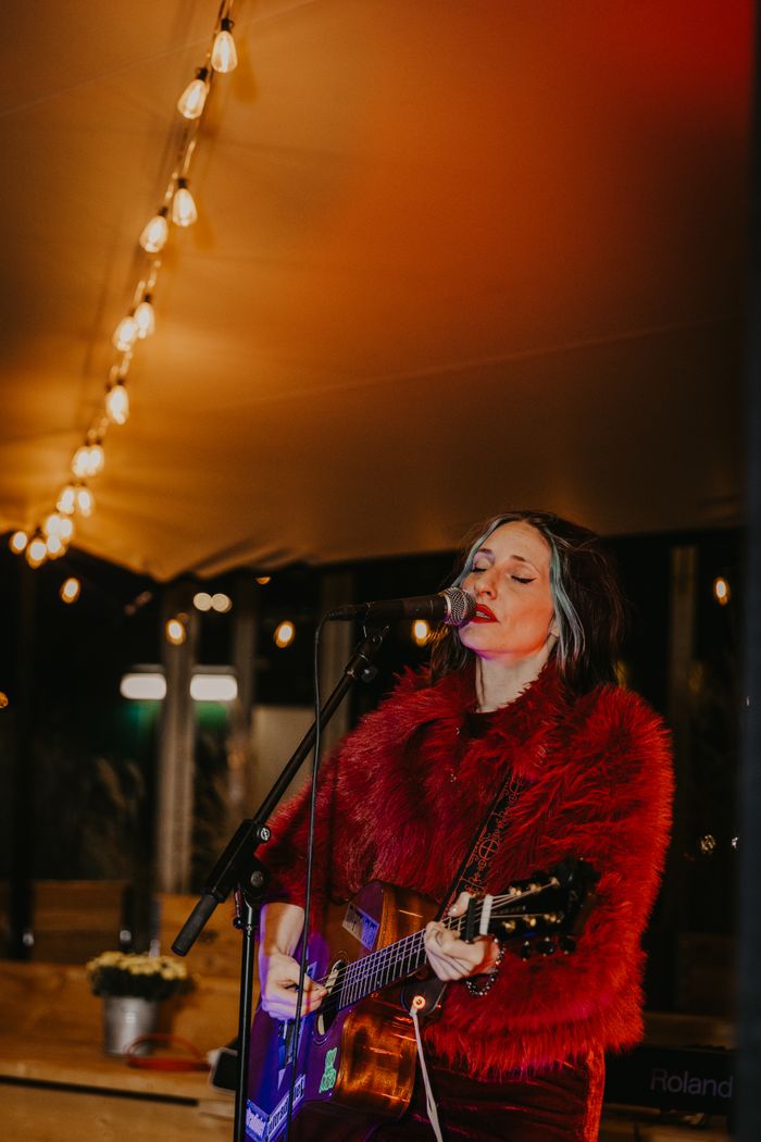 Female guitarist performing live under string lights in Berlin.