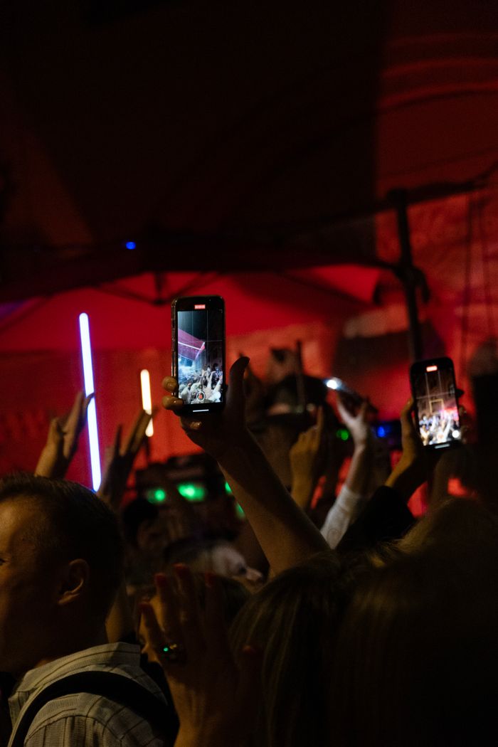 Energetic concert crowd holding smartphones to record the event under colorful lights.