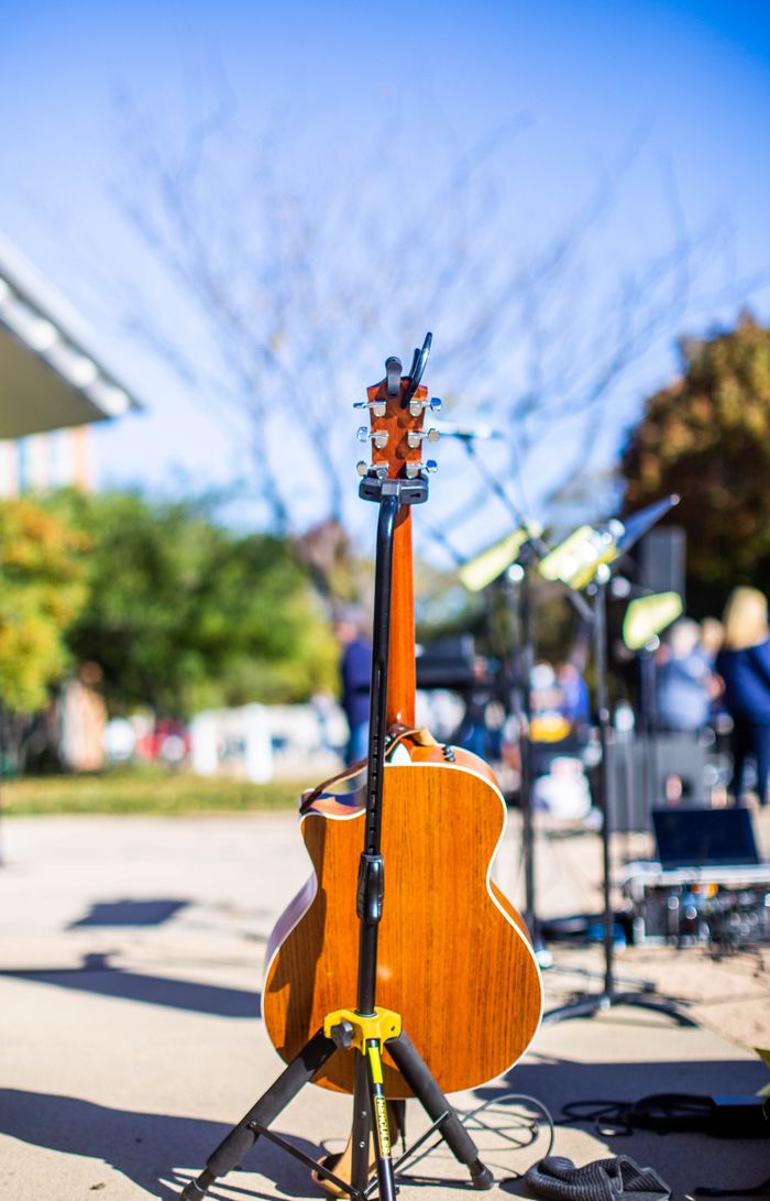 A wooden acoustic guitar on a stand in a sunlit park setting with blurred background.
