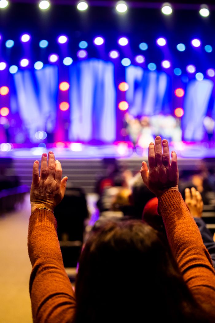 A lively concert scene with attendees raising hands in excitement, colorful stage lights.