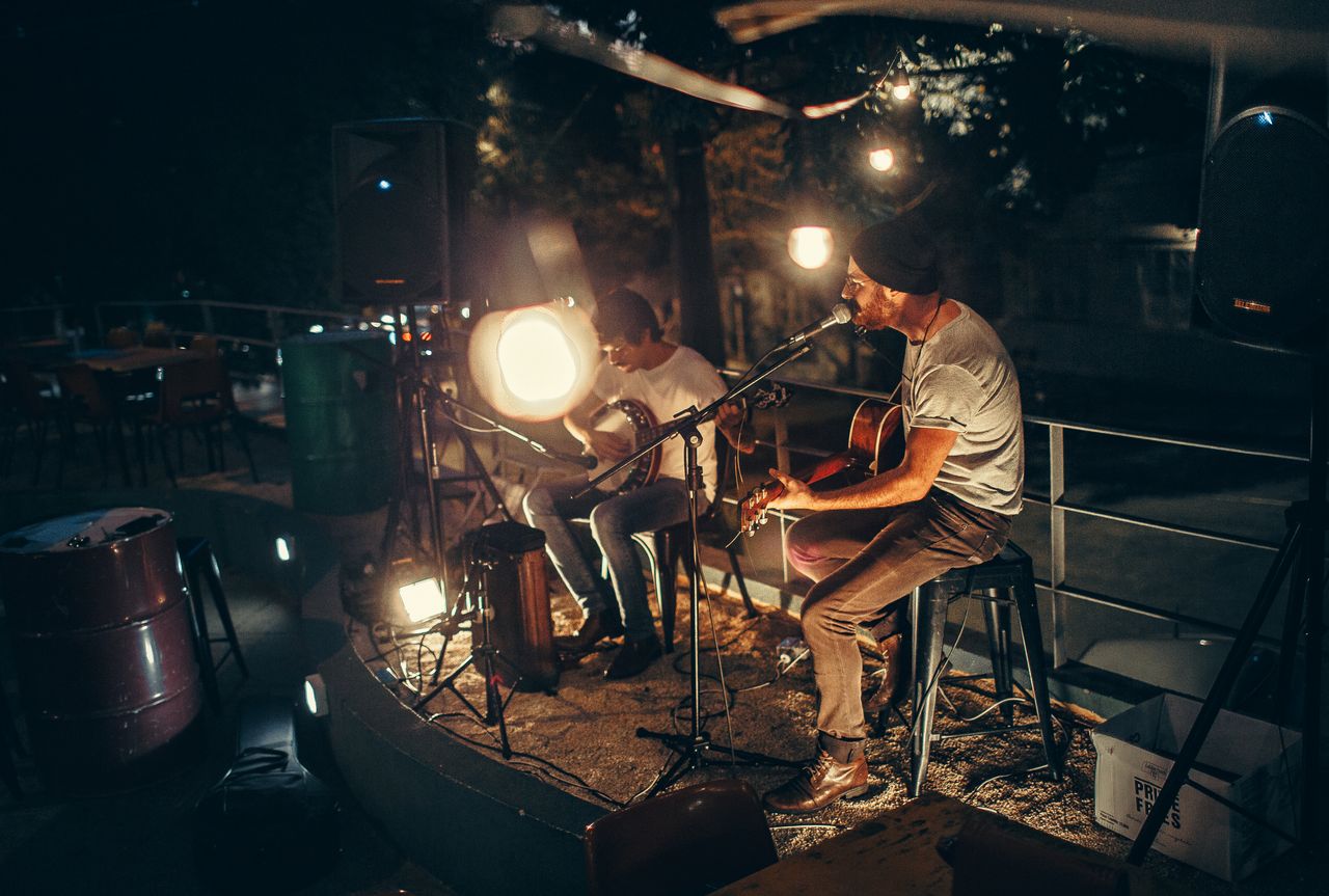 Two musicians performing acoustic music outdoors at night, illuminated by soft ambient lighting.