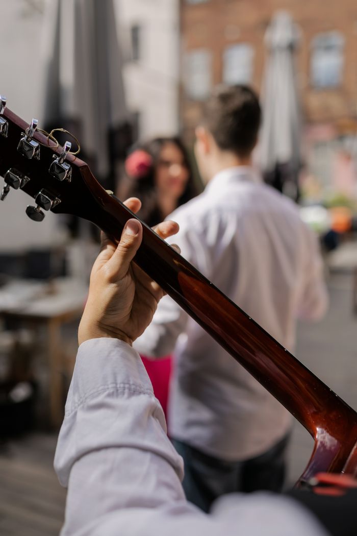 A close-up view of a guitarist playing outdoors in a lively urban setting.