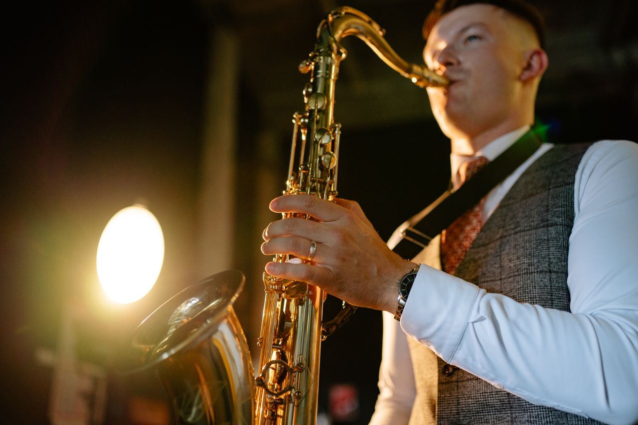 A young male saxophonist playing under warm stage lights indoors.